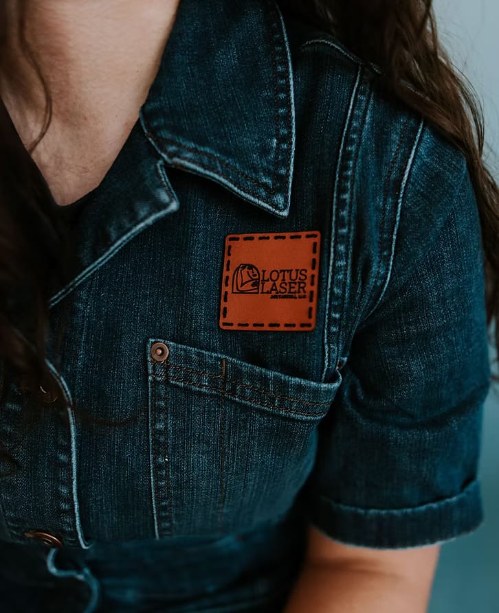 Close-up of a denim jacket with a brown leather Lotus Laser Aesthetics logo patch.